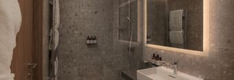 Modern bathroom at NH Collection Milano CityLife with gray stone tiles, wall-mounted towels, illuminated mirror, and sink with toiletries