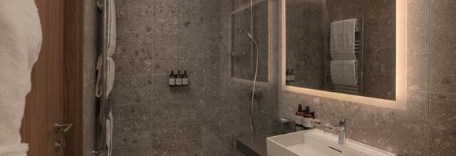 Modern bathroom at NH Collection Milano CityLife with gray stone tiles, wall-mounted towels, illuminated mirror, and sink with toiletries