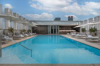 Outdoor rectangular swimming pool with light blue water, surrounded by grey lounge chairs and white umbrellas at NH Collection Milano CityLife