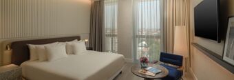 A modern hotel room at NH Collection Milano CityLife with a large bed, marble side table, blue armchair, and wall-mounted TV