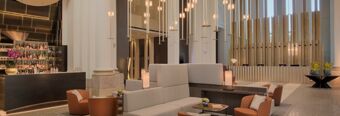 Contemporary lounge area with beige sofas, brown chairs, hanging pendant lights, and a bar at NH Collection Milano CityLife
