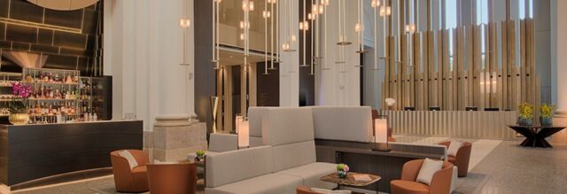 Contemporary lounge area with beige sofas, brown chairs, hanging pendant lights, and a bar at NH Collection Milano CityLife