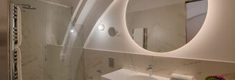 Modern bathroom with a backlit circular mirror, marble walls, glass shower door, and towels at NH Collection Milano CityLife