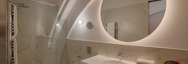 Modern bathroom with a backlit circular mirror, marble walls, glass shower door, and towels at NH Collection Milano CityLife