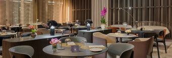 Modern dining area at NH Collection Milano CityLife featuring round tables, various chairs, decorative flowers, and ambient lighting