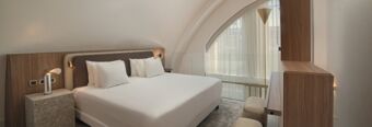 Bedroom interior at NH Collection Milano CityLife featuring a large bed with white linens, wooden furniture, and a large arched window