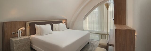 Bedroom interior at NH Collection Milano CityLife featuring a large bed with white linens, wooden furniture, and a large arched window