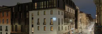 Hotel NH Milano Corso Buenos Aires building illuminated at dusk with surrounding architecture and street full of cars and lights