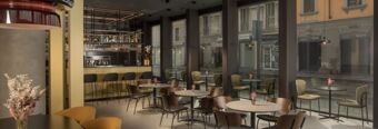 Modern bar and seating area with round tables, chairs, large windows showing street outside at Hotel NH Milano Corso Buenos Aires