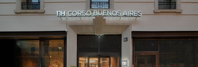 Entrance of Hotel NH Milano Corso Buenos Aires with illuminated sign above glass double doors and large windows on both sides
