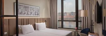 Twin beds with white sheets and pillows in a hotel room at Hotel NH Milano Corso Buenos Aires with a large window and city view