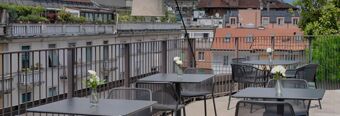 Outdoor seating area with black tables and mesh chairs on a terrace overlooking buildings at Hotel NH Milano Corso Buenos Aires