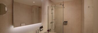 Modern bathroom in Hotel NH Milano Corso Buenos Aires with large mirror, glass shower, tiled walls, and mounted toiletries