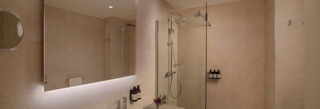Modern bathroom in Hotel NH Milano Corso Buenos Aires with large mirror, glass shower, tiled walls, and mounted toiletries
