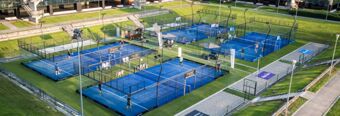 Four blue padel tennis courts with players and a green lawn surrounding them at NH Milano Congress Centre outdoor area