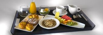 Breakfast tray with croissants, cereal, sliced fruits, orange juice, water, tea cup, and utensils at NH Milano Congress Centre