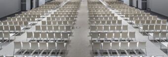 Rows of white chairs neatly arranged in a large, empty conference room at NH Milano Congress Centre with carpeted flooring