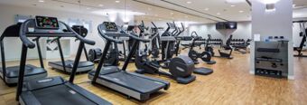 Gym room at NH Milano Congress Centre with treadmills, exercise bikes, rowing machines, and a rack of dumbbells along a mirrored wall