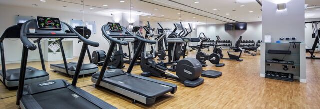 Gym room at NH Milano Congress Centre with treadmills, exercise bikes, rowing machines, and a rack of dumbbells along a mirrored wall