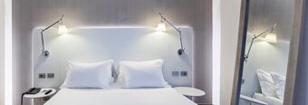 A modern hotel room at NH Milano Congress Centre featuring a double bed with white pillows and bedside tables with lamps on a light wood wall