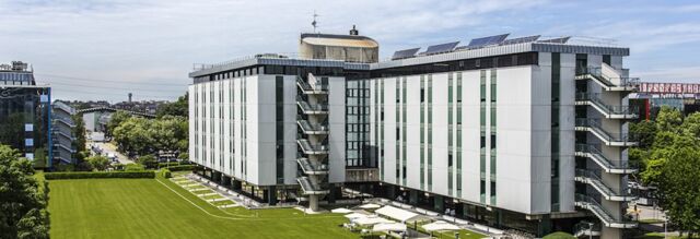 Large modern building with glass and white panels surrounded by green lawn and umbrellas at NH Milano Congress Centre