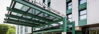 Glass and metal canopy entrance with green beams at NH Milano Congress Centre building under a cloudy sky