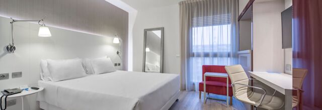 A modern hotel room at NH Milano Congress Centre with a large bed, white linens, wall lamps, a red chair, desk, and window with curtains