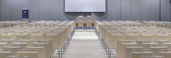 Empty conference room at NH Milano Congress Centre with rows of beige chairs facing a stage and projector screen