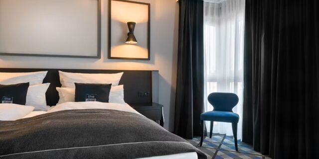 Modern eingerichtetes Hotelzimmer mit Doppelbett, indirekter Beleuchtung und blauem Stuhl vor Fenster im Holiday Inn - the niu, Square Mannheim.
