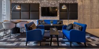 Moderner und stilvoll eingerichteter Aufenthaltsbereich mit blauen Sesseln, Fernseher und Esstisch im Holiday Inn - the niu, Square Mannheim.