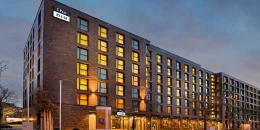 Abendaufnahme der Fassade vom Hotel Holiday Inn - the niu, Square Mannheim mit beleuchteten Fenstern und modernem Backstein-Design.