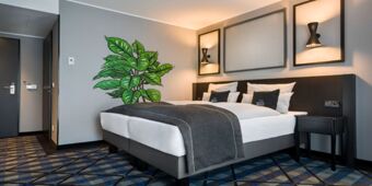 Modern eingerichtetes Hotelzimmer mit Doppelbett, Nachttisch, Wandlampen und gro&szlig;er Topfpflanze im Holiday Inn - the niu, Square Mannheim.
