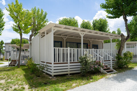 White wooden cabins with covered porches surrounded by green trees and plants at Rimini Family Resort under blue sky