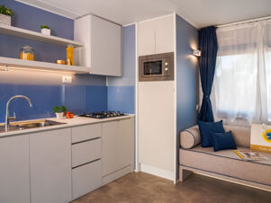 Modern kitchen area at Rimini Family Resort with white cabinets, gas stove, built-in microwave, sink, and a small seating area by the window