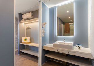 Modern bathroom and closet area with illuminated mirror, white sink, hairdryer, and branded items at Romagna Family Resort
