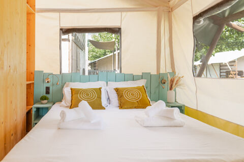 Bed with white sheets and mustard yellow pillows inside a canvas tent with light blue headboard at Romagna Family Resort