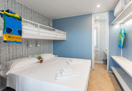 A hotel room at Romagna Family Resort with a double bed, bunk bed, folded towels, and a blue wall with patterned wallpaper