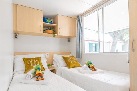 Two single beds with white bedding and yellow pillows with circular patterns inside a room at Riccione Easy Camping Village with a window and wooden cabinets above the beds