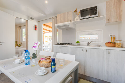 Dining table with snacks, cups, water bottles, and a modern kitchen with stove, microwave, and sink at Riccione Easy Camping Village