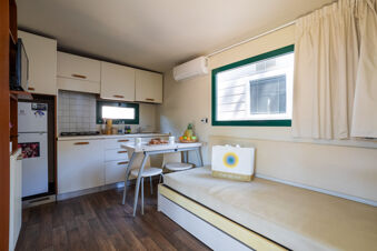 Compact kitchen and dining area with white cabinets, a small table with stools, and a seating bench in Adriano Family Collection