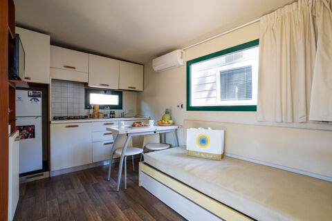 Compact kitchen and dining area with white cabinets, a small table with stools, and a seating bench in Adriano Family Collection
