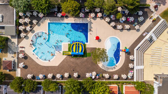 Aerial view of Marina Family Resort outdoor area with three swimming pools including a water slide and numerous umbrellas with sunbeds around the pools