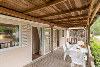 Wooden patio with white plastic chairs and table set with breakfast items outside rooms at Marina Family Resort
