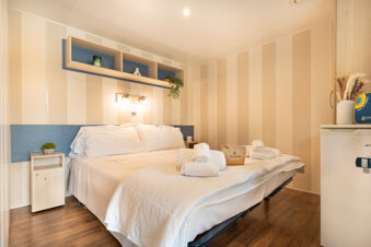 Double bed with white linens and towels in a hotel room with beige striped walls and wooden floors at Marina Family Resort
