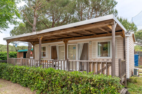 Wooden veranda with a table and chairs in front of a beige cabin surrounded by greenery at Marina Family Resort