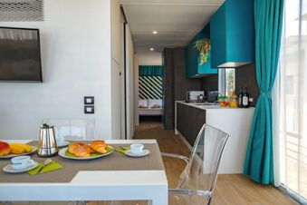 Dining table with croissants and fruit next to a kitchenette with teal cabinets and curtains at Pini Boutique Resort