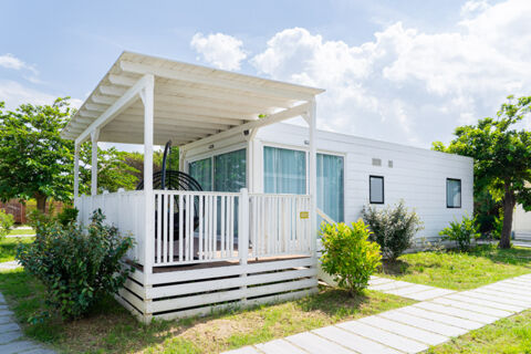 White modern cabin with a covered porch and hanging chairs surrounded by green trees and plants at Pini Boutique Resort