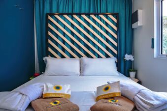 Bed with two white pillows and wooden headboard against blue curtains beside a window in Pini Boutique Resort room