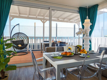 Dining area at Pini Boutique Resort with transparent chairs, a table set with coffee cups and croissants, and an outdoor hanging chair visible through glass doors