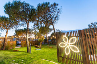 Green lawn with pine trees, hammocks, string lights, wooden fence, and illuminated flower decoration at Pini Boutique Resort